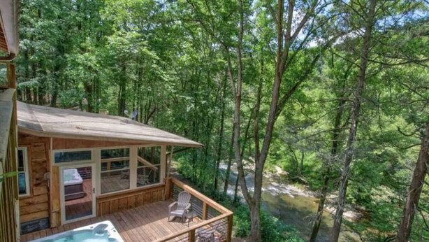 Eine Holzhütte mit Whirlpool, Terrasse und Blick auf ein bewaldetes Gebiet.