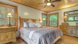 Ein Schlafzimmer mit Holzboden, einem Bett mit Kopfteil, zwei Fenstern, einem Deckenventilator und Holzmöbeln.