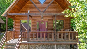 Eine Blockhütte mit Stein Fundament, einer Holzterrasse und einer roten Tür.