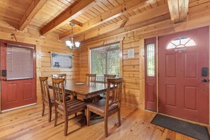 A wooden cabin interior with a dining table, chairs, a chandelier, and a red door with a 'No Smoking' sign. - White Oak 212 (Gatlinburg)