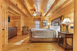 A wooden cabin bedroom with a bed, nightstands, a dresser, a ceiling fan, and a window. - White Oak 212 (Gatlinburg)