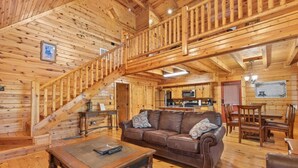 Innenansicht einer Holzhütte mit Treppe, einem Wohnzimmer mit Sofa und Couchtisch sowie einer Küchenzeile.