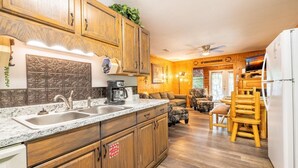 Una cocina con armarios de madera, encimera de mármol, cafetera y comedor con mesa y sillas de madera.