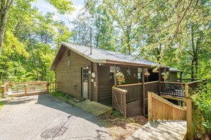 Eine kleine Holzhütte mit Veranda, Terrasse und umzäunter Auffahrt.
