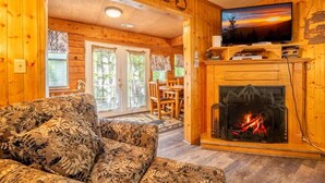 Interior de una cabaña de troncos con chimenea, televisor y un sofá estampado.
