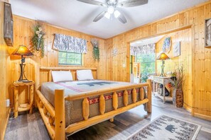 Ein Schlafzimmer in einer Holzhütte mit einem Bett, einem Deckenventilator und einem Fenster.