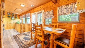 Un interior de madera con una mesa de comedor, sillas y ventanas con cortinas.