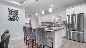 Una cocina moderna con armarios blancos, un refrigerador de acero inoxidable y una zona de bar con sillas tapizadas.