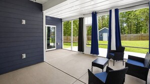 Un patio cubierto con mobiliario exterior, puertas correderas de vidrio y vista al jardín trasero.