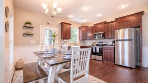 A modern kitchen with wooden cabinets, stainless steel appliances, and a dining area with white chairs and a wooden table. - Fabulous Farmhouse (Sevierville)
