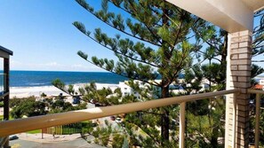 Un balcó amb vista a l'oceà i a la platja, envoltat d'arbres i edificis.