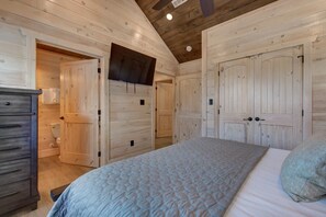 A bedroom with wooden walls, a bed with a quilt, a dresser, and a door leading to another room. - Summit View (Sevierville)