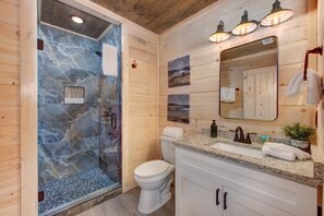 A bathroom with a glass-enclosed shower, a white toilet, a granite countertop sink, and a mirror above the sink. - Summit View (Sevierville)