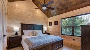 Une chambre avec un plafond en bois, un lit avec une tête de lit, deux tables de chevet avec des lampes et une fenêtre avec des stores.