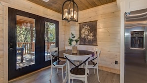 Un intérieur en bois comprenant une table à manger, des chaises, un lustre, un réfrigérateur et une porte donnant sur une terrasse extérieure.