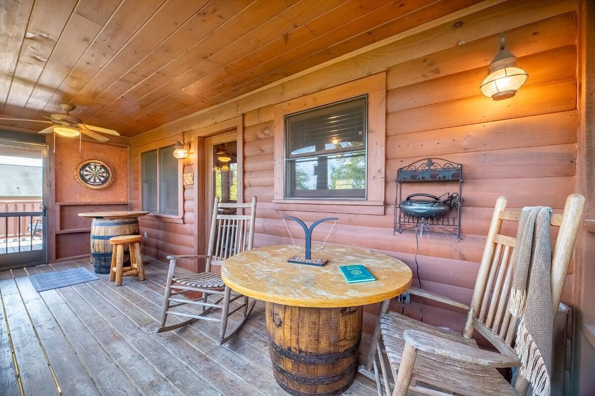 A wooden cabin with a round table, chairs, a dartboard, and a ceiling fan.