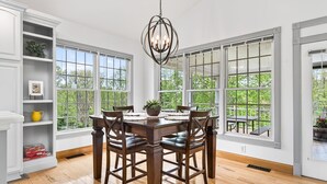 Un comedor con mesa y sillas de madera, ventanas amplias y una lámpara de araña.