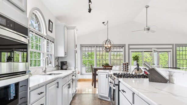Una cocina moderna con armarios blancos, una isla central, una estufa y ventanas amplias.