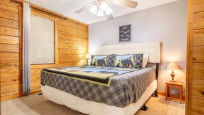 A bedroom with a bed, a ceiling fan, a wall-mounted light, a window with blinds, and a sign on the wall. - Z - Lone Wolf (Sevierville)