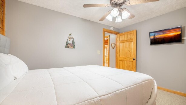 A bedroom with a bed, a ceiling fan, a door, and a wall-mounted TV. - Z - Lone Wolf (Sevierville)