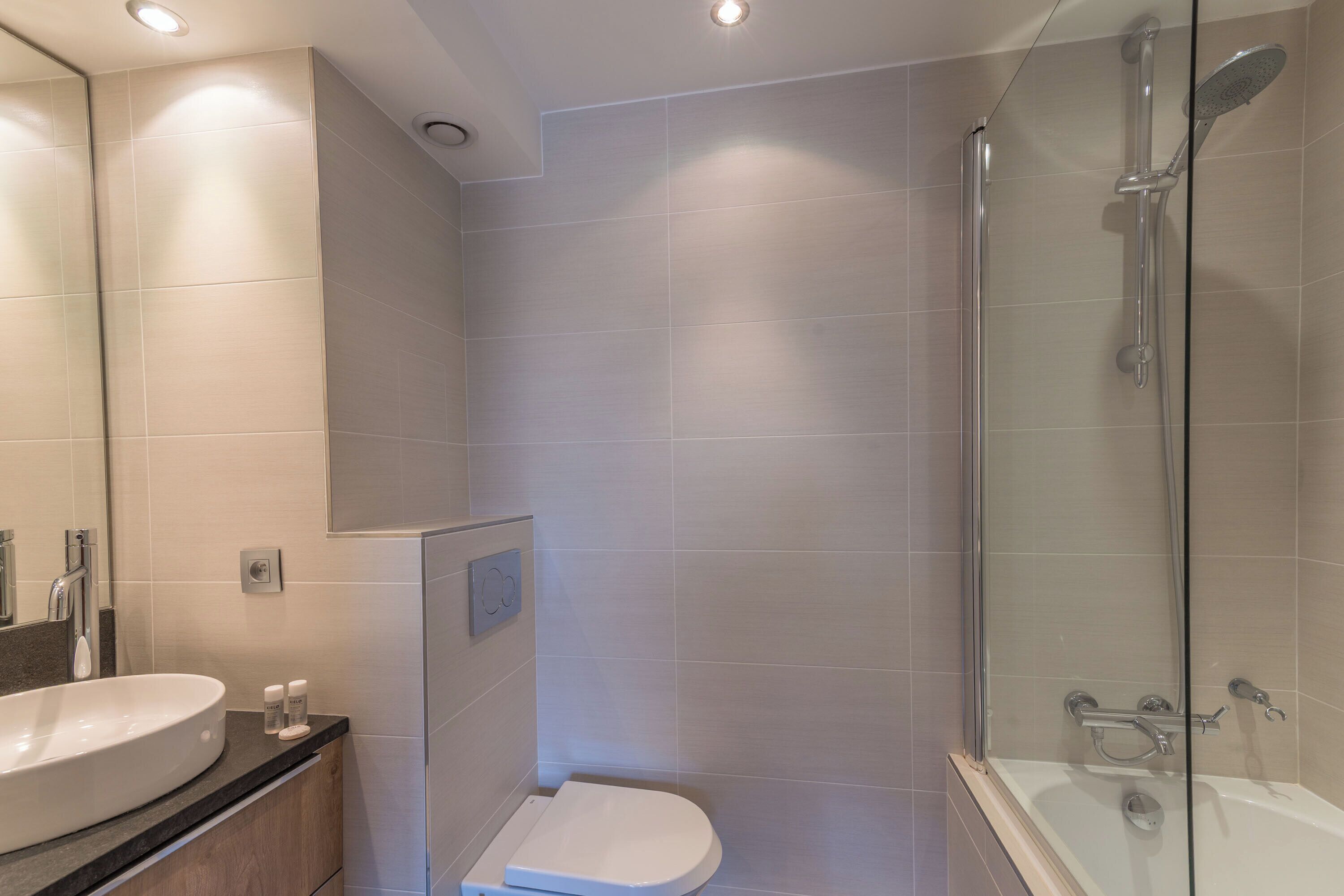 Un baño moderno con lavamanos, inodoro y ducha con mampara de vidrio.