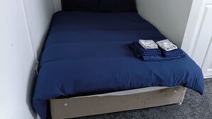 A single bed with a dark blue bedspread, two pillows, and a folded towel on the footboard.