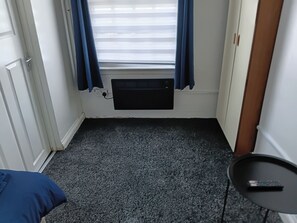 A room with a carpeted floor, a radiator, a door, and a small table with a remote control. - Studio Sleeps 2 With Parking (Oldbury)