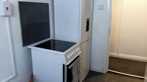 A compact kitchenette with a built-in oven and microwave, a small refrigerator, and a black tile backsplash.