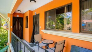 Ein Balkon mit zwei Stühlen und einem kleinen Tisch, ein Fenster mit Vorhängen und eine Tür mit einer Nummer.