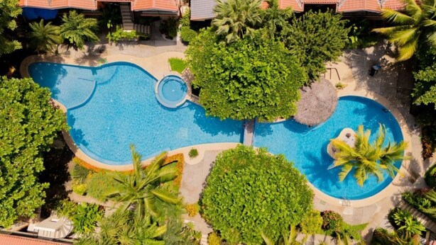 An aerial view of a resort with a large swimming pool surrounded by lush greenery and palm trees. - Cocomarindo 66 - Stylishly Renovated 1BR (Guanacaste Province)