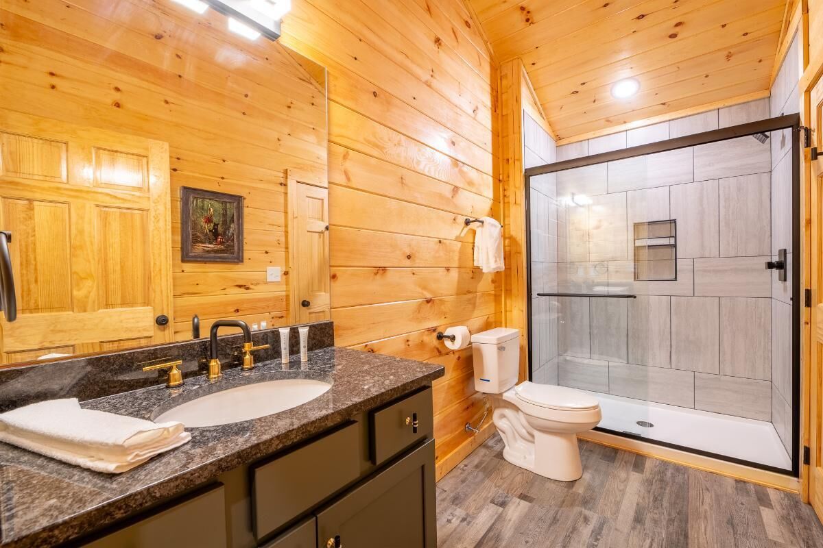 Une salle de bain rustique, aménagée dans une cabane en bois, avec un lavabo, des toilettes et une douche à parois de verre.