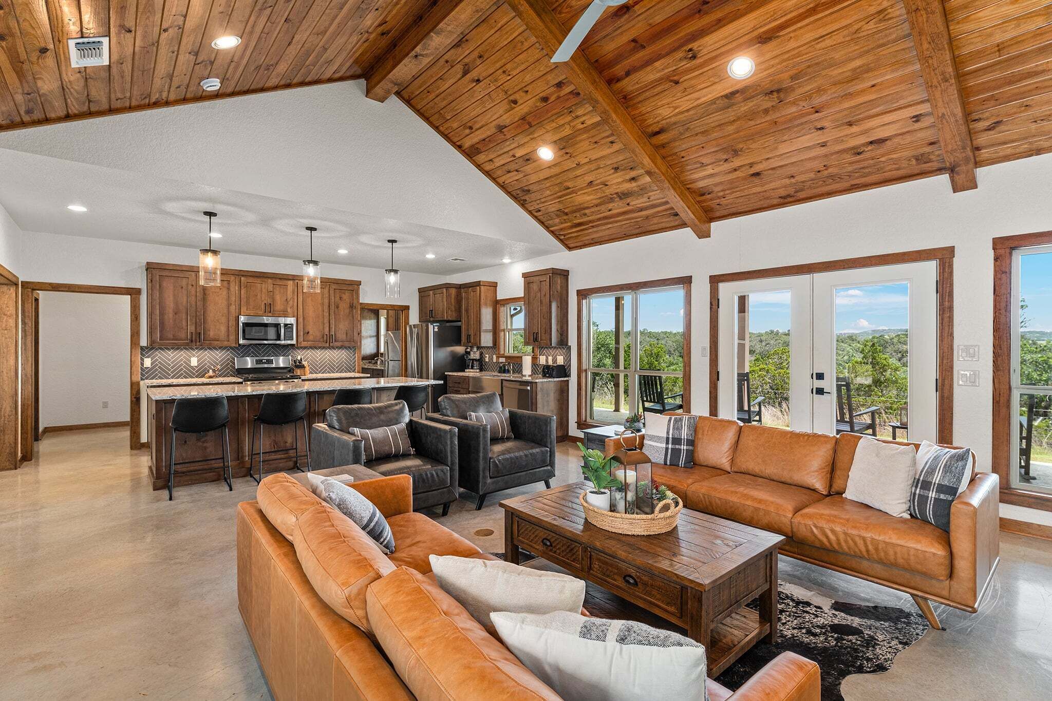 A spacious living area with a kitchen, wooden ceiling, and large windows.
