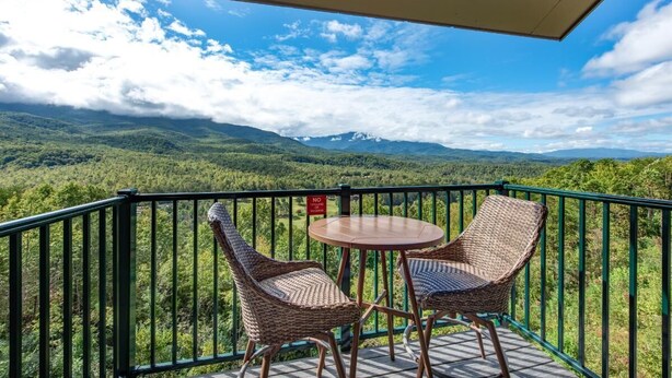 A balcony with wicker chairs and a small table, overlooking a mountainous landscape. - Teetop Getaway (Gatlinburg)