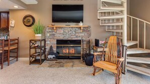 A living room with a stone fireplace, a mounted TV, a wooden chair, and a staircase. - Teetop Getaway (Gatlinburg)