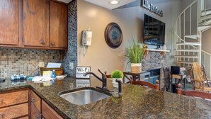 A kitchen with granite countertops, a sink, wooden cabinets, a Wi-Fi sign, a clock, and a stone fireplace. - Teetop Getaway (Gatlinburg)