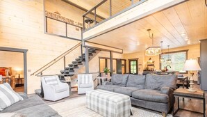 Un interior moderno con una escalera, sofás grises, un reposapiés a cuadros y una zona de cocina.