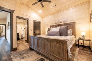 A wooden-paneled bedroom with a large bed, a ceiling fan, and a nightstand with a lamp. - Autumn Bear (Sevierville)