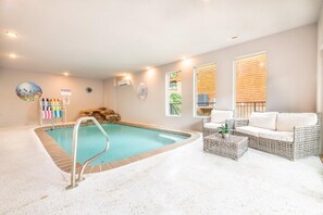 A pool area with a lounge chair and a small table, a wall-mounted air conditioner, and a window with blinds. - Autumn Bear (Sevierville)