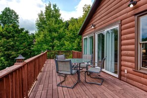 A wooden deck with a table and chairs, surrounded by a wooden railing and glass doors. - Z - Bear Pause Retreat (Sevierville)