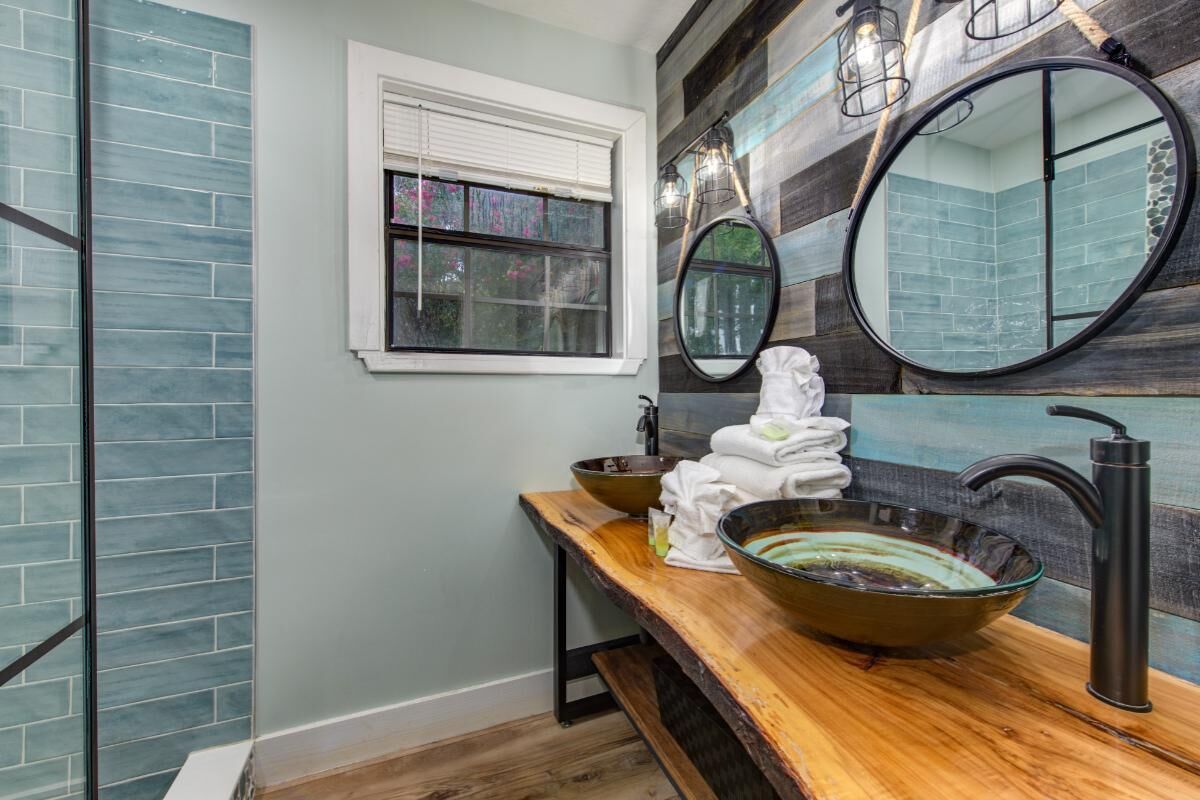 A bathroom with a wooden vanity, a large mirror, and a glass bowl sink.