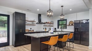 Una cocina moderna con armarios oscuros, una isla central con taburetes de bar, electrodomésticos de acero inoxidable e iluminación colgante.