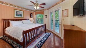 Un dormitorio con una cama de madera, un ventilador de techo, un televisor y vistas al exterior.