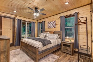 Quarto de cabana de madeira com cama, mesa de cabeceira e ventoinha no teto.