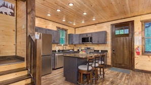 A wooden cabin interior with a kitchen, bar area, and a door with a window. - Dreamcatcher Lodge (Sevierville)