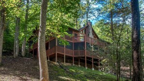 A cabin with a wooden deck, surrounded by trees. - Sage Grass Retreat (Sevierville)