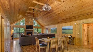 A wooden cabin interior with a fireplace, dining area, and large windows. - Sage Grass Retreat (Sevierville)