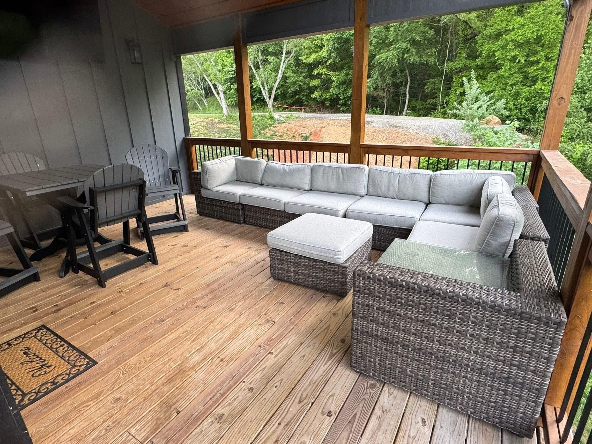 A covered outdoor seating area with a wooden deck, a sofa, a table, and chairs.
