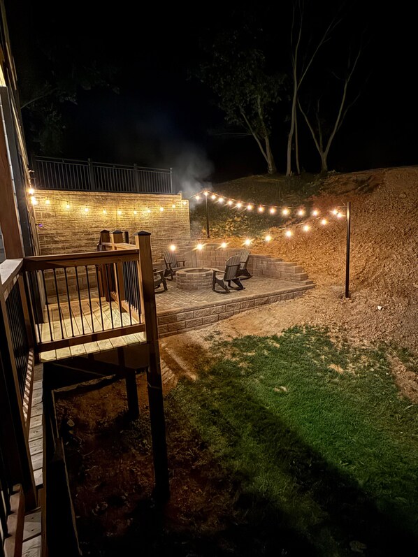 Un patio con mobiliario exterior, una fogata y luces colgantes.