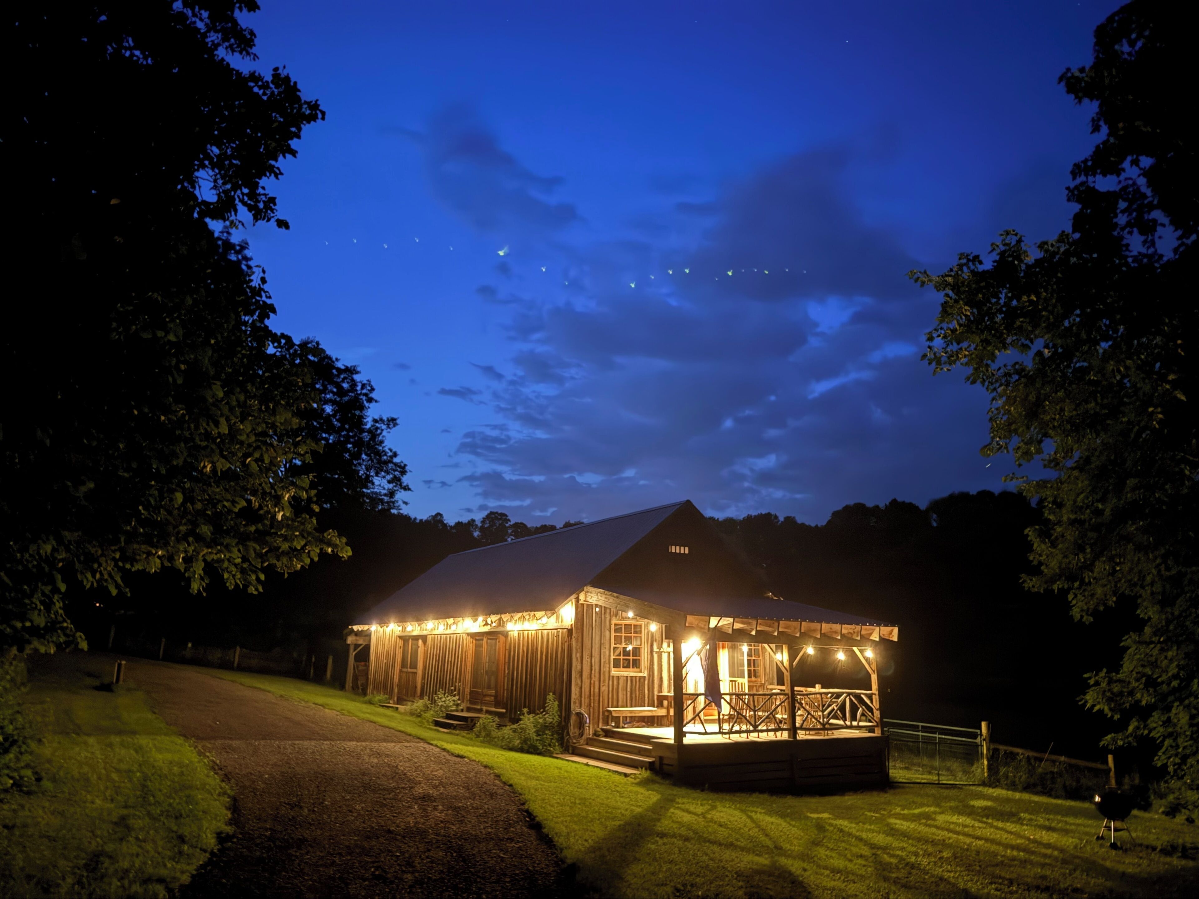 A wooden cabin with a porch, surrounded by trees, under a night sky.
