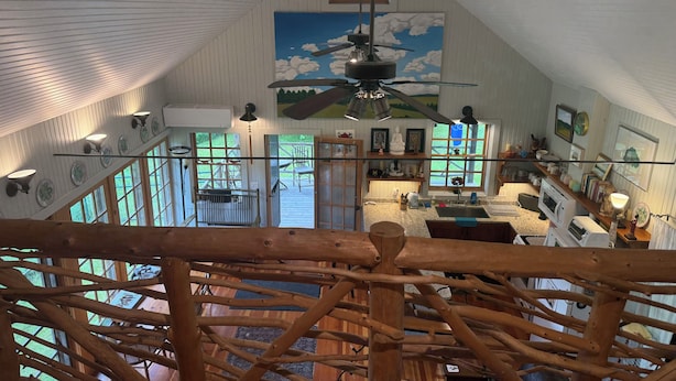 Een rustiek interieur met houten plafond, een plafondventilator en uitzicht op het buitengebied door grote ramen.